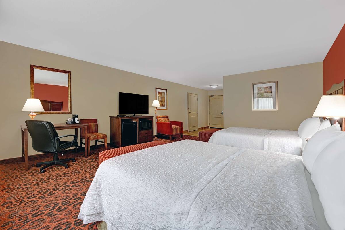 A hotel room with two beds, a desk with a chair, a television, and a small table.