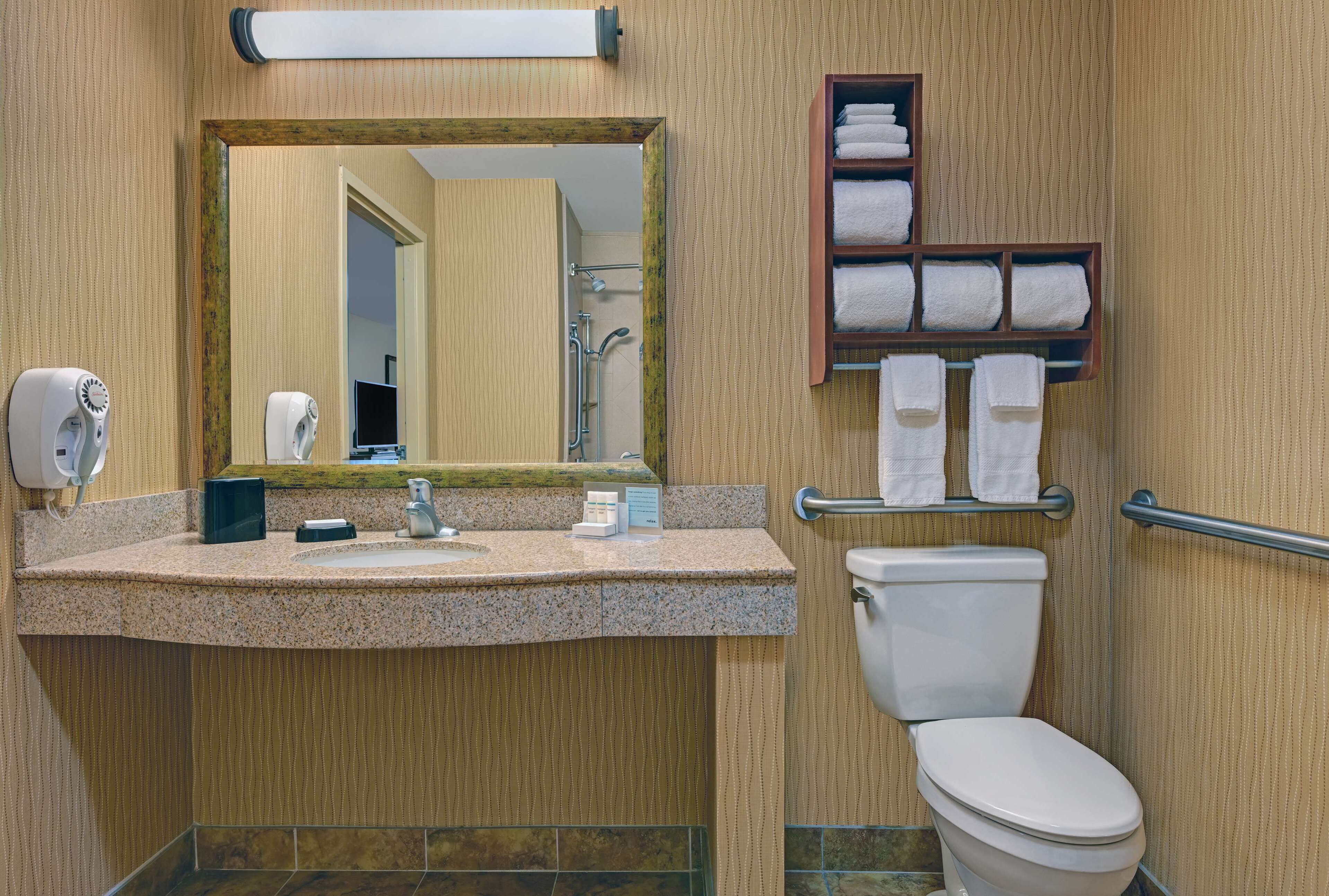 A bathroom with a granite countertop, a white toilet, a mirror, a towel rack, and a hand dryer.
