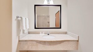 Un baño con lavamanos de encimera de granito, un espejo con marco negro y un perchero con dos toallas blancas.