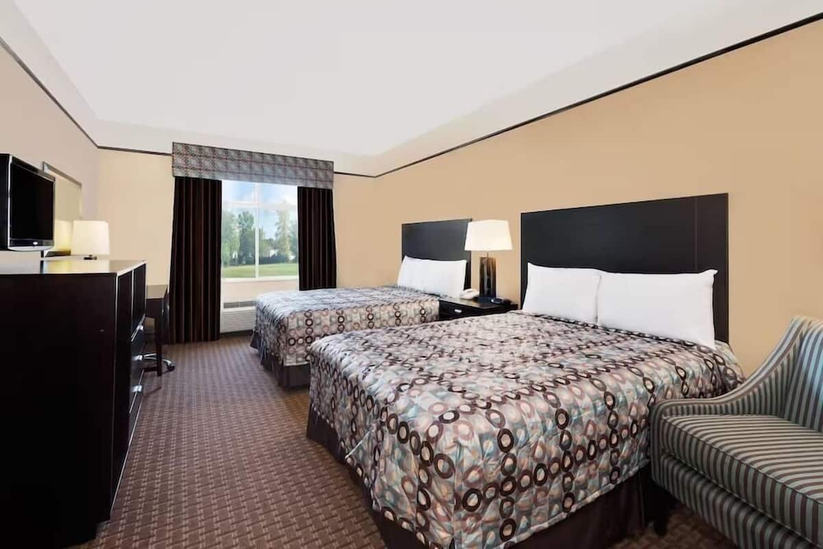 Une chambre d’hôtel avec deux lits, un bureau avec une télévision, une chaise et une fenêtre avec des rideaux.
