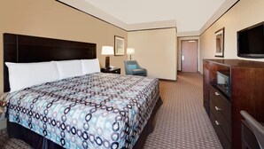 Una habitación de hotel con una cama grande, un escritorio con lámpara, una silla, un televisor y un aparador.
