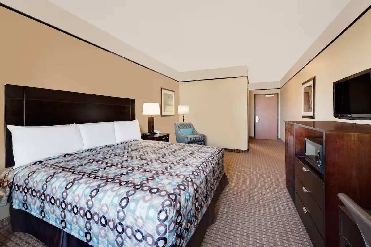 Une chambre d’hôtel avec un grand lit, un bureau avec une lampe, une chaise, une télévision et une commode.