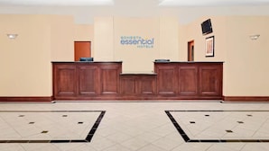Un área de recepción con un mostrador de madera, un cartel de Sonesta Essential Hotels y un suelo de baldosas con un diseño geométrico.