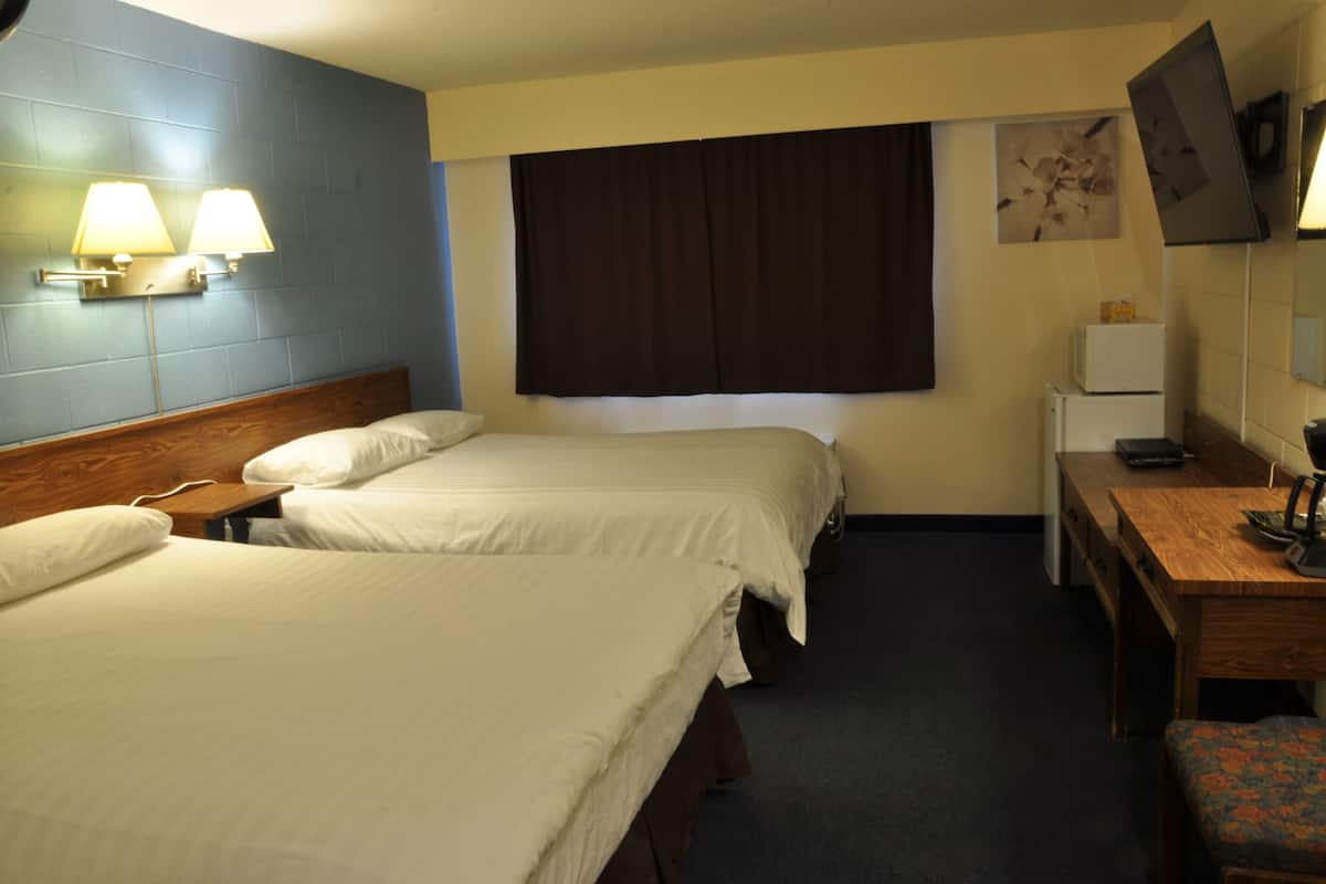 A hotel room with two beds, a desk, a chair, a TV, and a small refrigerator.