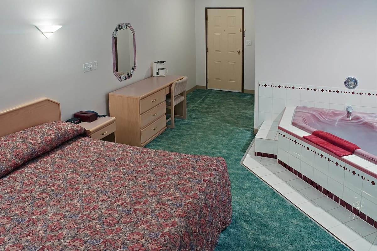 A bedroom with a bed, a dresser, a mirror, a coffee maker, and a bathroom with a bathtub.