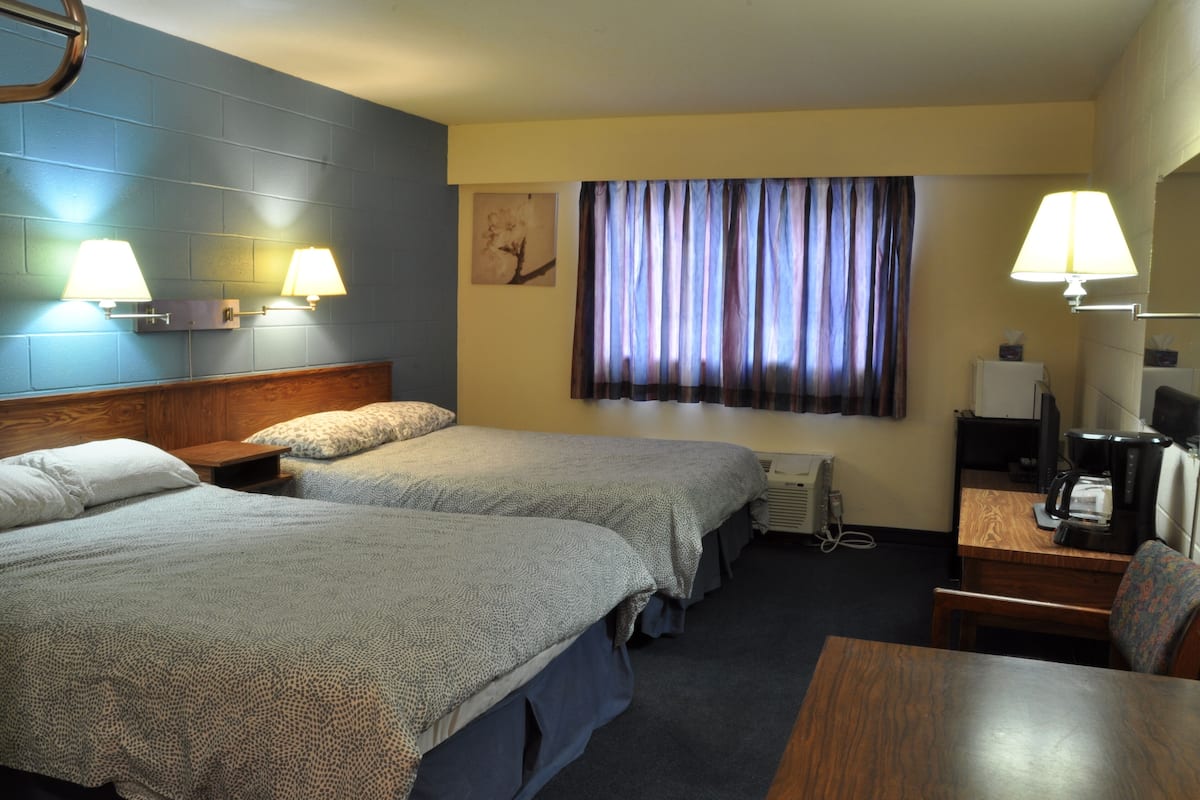 A hotel room with two beds, a desk with a chair, a coffee maker, and a TV.