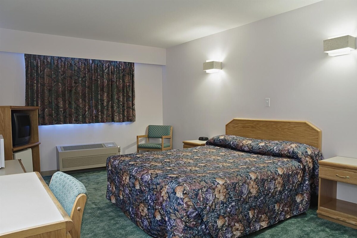 A hotel room with a bed, a chair, a desk, a television, and a window with curtains.
