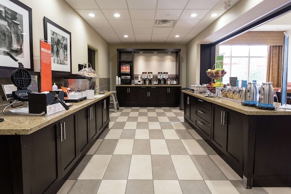 A modern kitchen with checkered flooring, dark cabinets, and a central island with coffee machines and fruit. - Hampton Inn by Hilton Elliot Lake, Ontario (Elliot Lake)