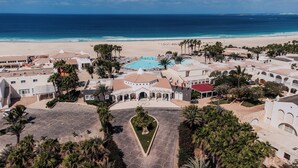 Un resort con piscina central, palmeras y vista al mar.