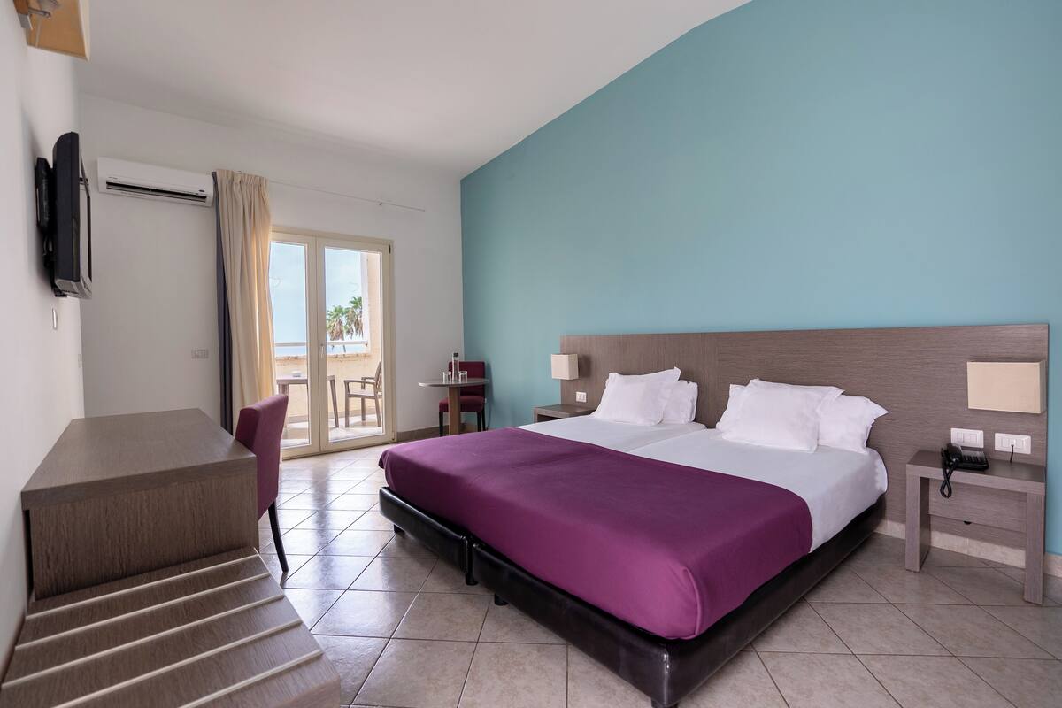 A hotel room with a bed, a desk, a chair, a TV, and a phone on a nightstand.