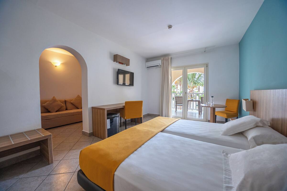 A hotel room with two beds, a desk, a sofa, and a balcony with a table and chairs.
