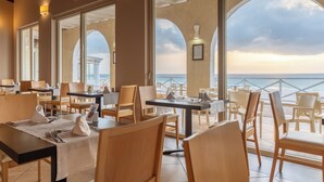 A restaurant with tables and chairs, large windows, and a view of the sea. - VOI Praia de Chaves Resort - All inclusive (Boa Vista)