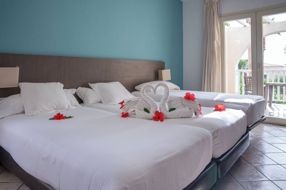 A hotel room with two beds, a teal wall, and a balcony with a view.