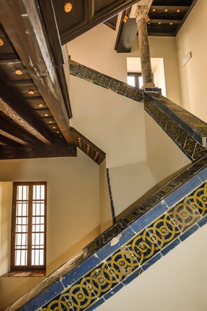 A spiral staircase with blue and yellow patterned tiles, wooden beams, and a window with a grid pattern.