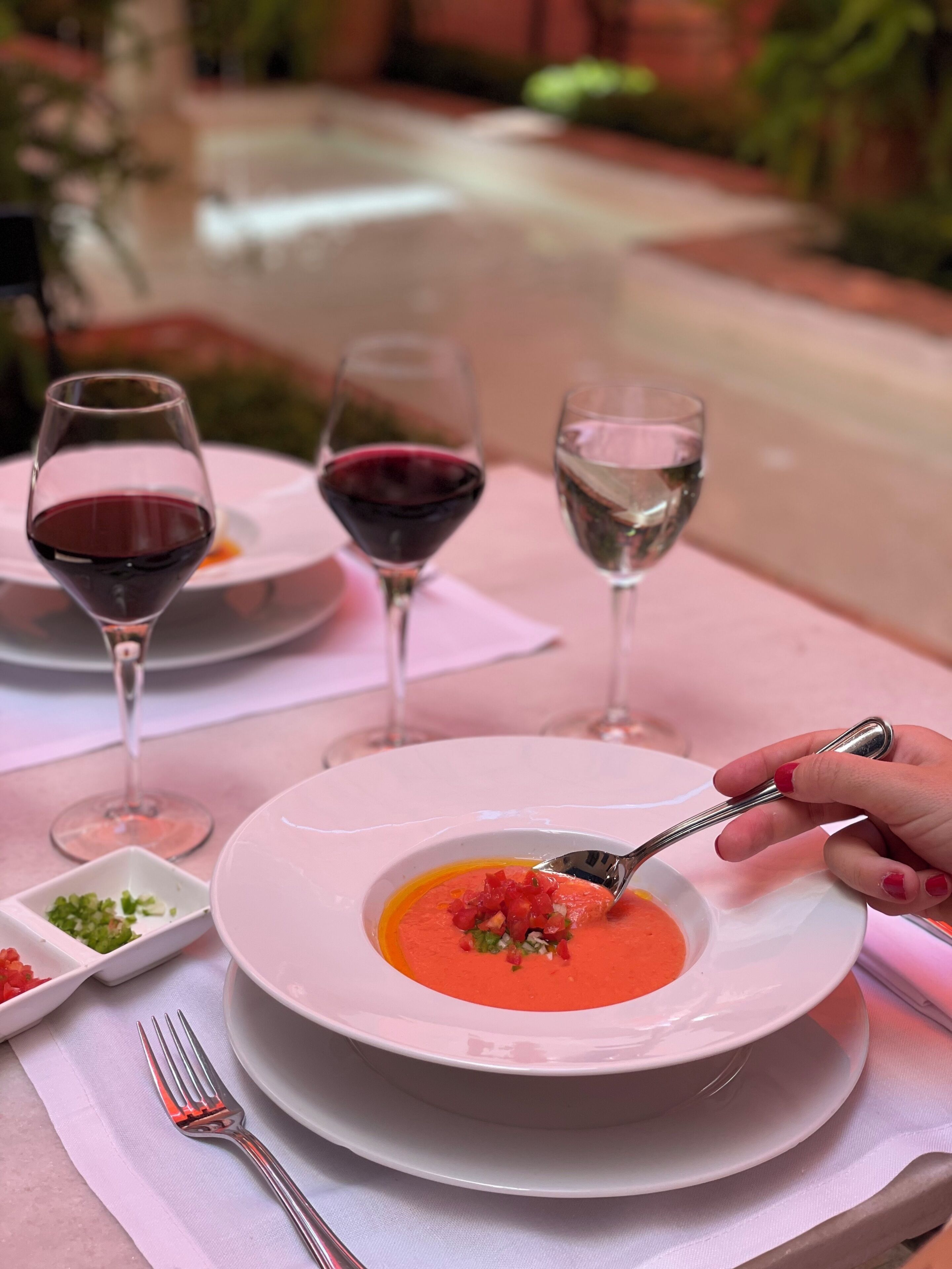 A dining table with a bowl of soup, a fork, and two wine glasses.