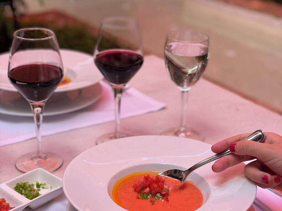 A dining table with a bowl of soup, a fork, and two wine glasses.