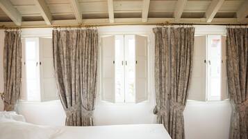 Une chambre à coucher avec un lit, deux fenêtres avec volets et des rideaux à motifs.