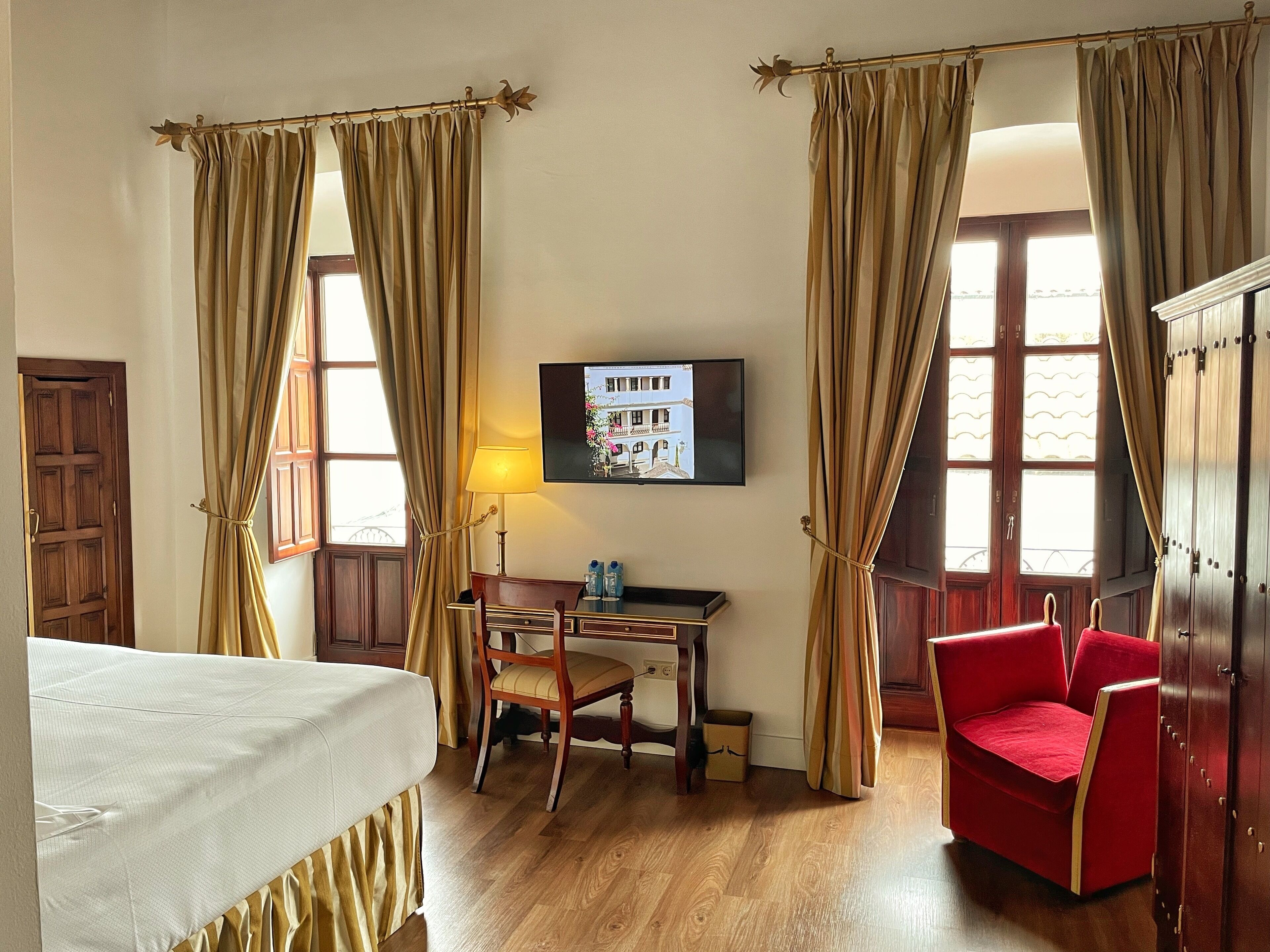 Une chambre d’hôtel avec un lit, un bureau et une chaise, une télévision et un fauteuil rouge.