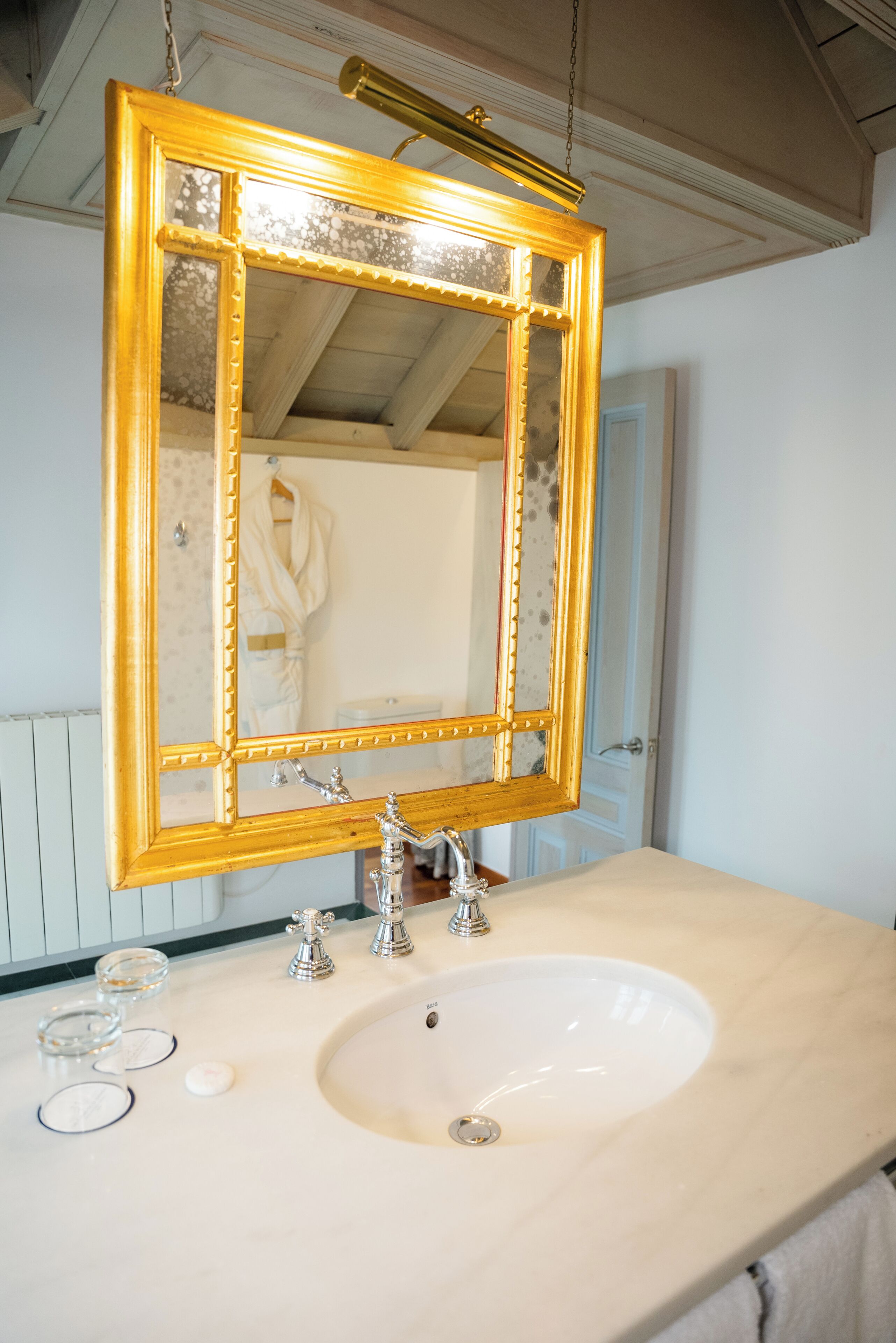 Un baño con un espejo grande con marco dorado, un lavabo blanco y dos llaves.