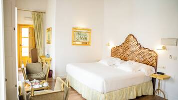 A hotel room with a large bed, a chair, a small table with breakfast, and a painting on the wall.