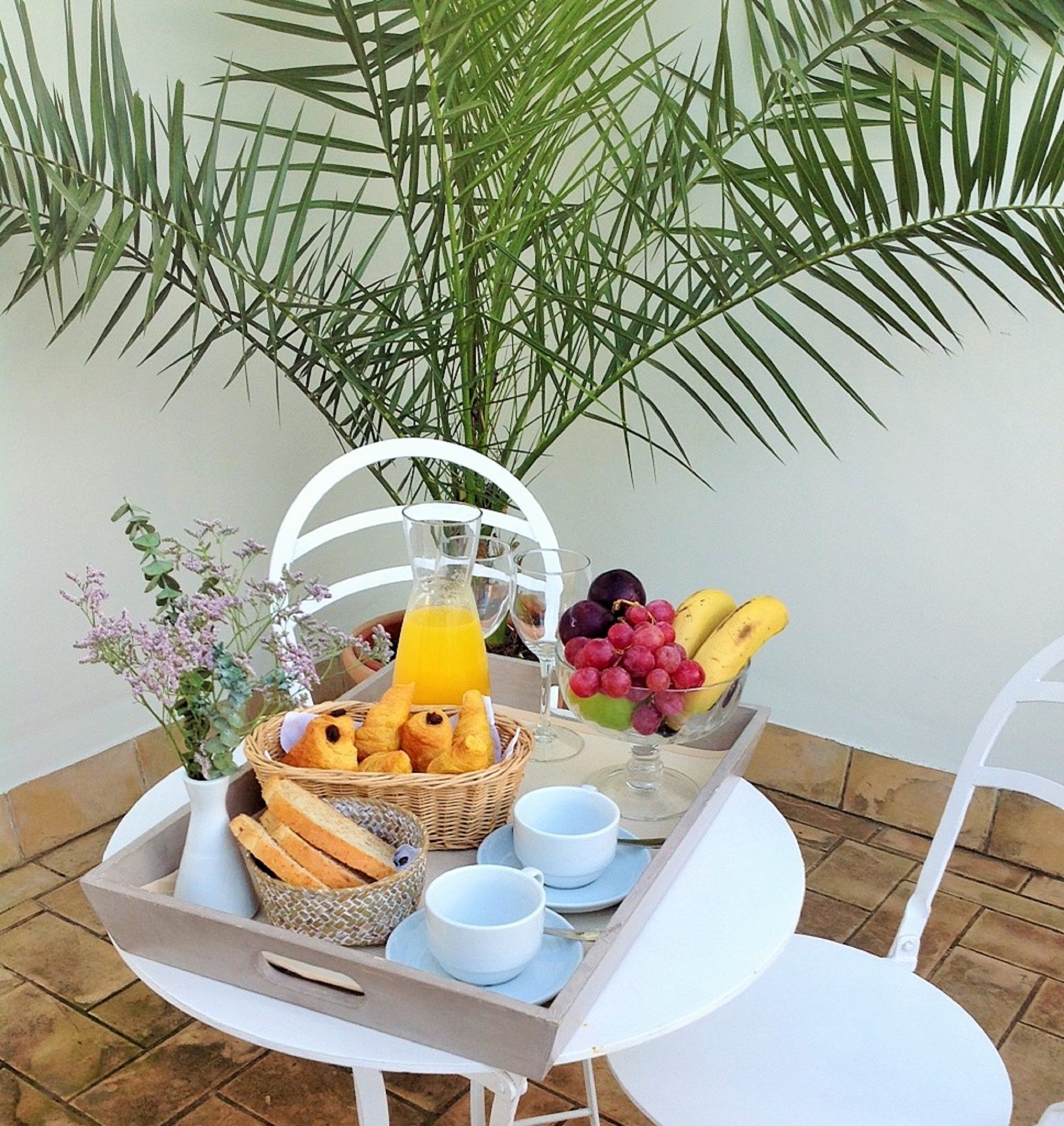 A breakfast tray with bread, fruits, and juice on a table with a chair.