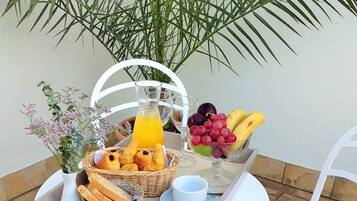 A breakfast tray with bread, fruits, and juice on a table with a chair.