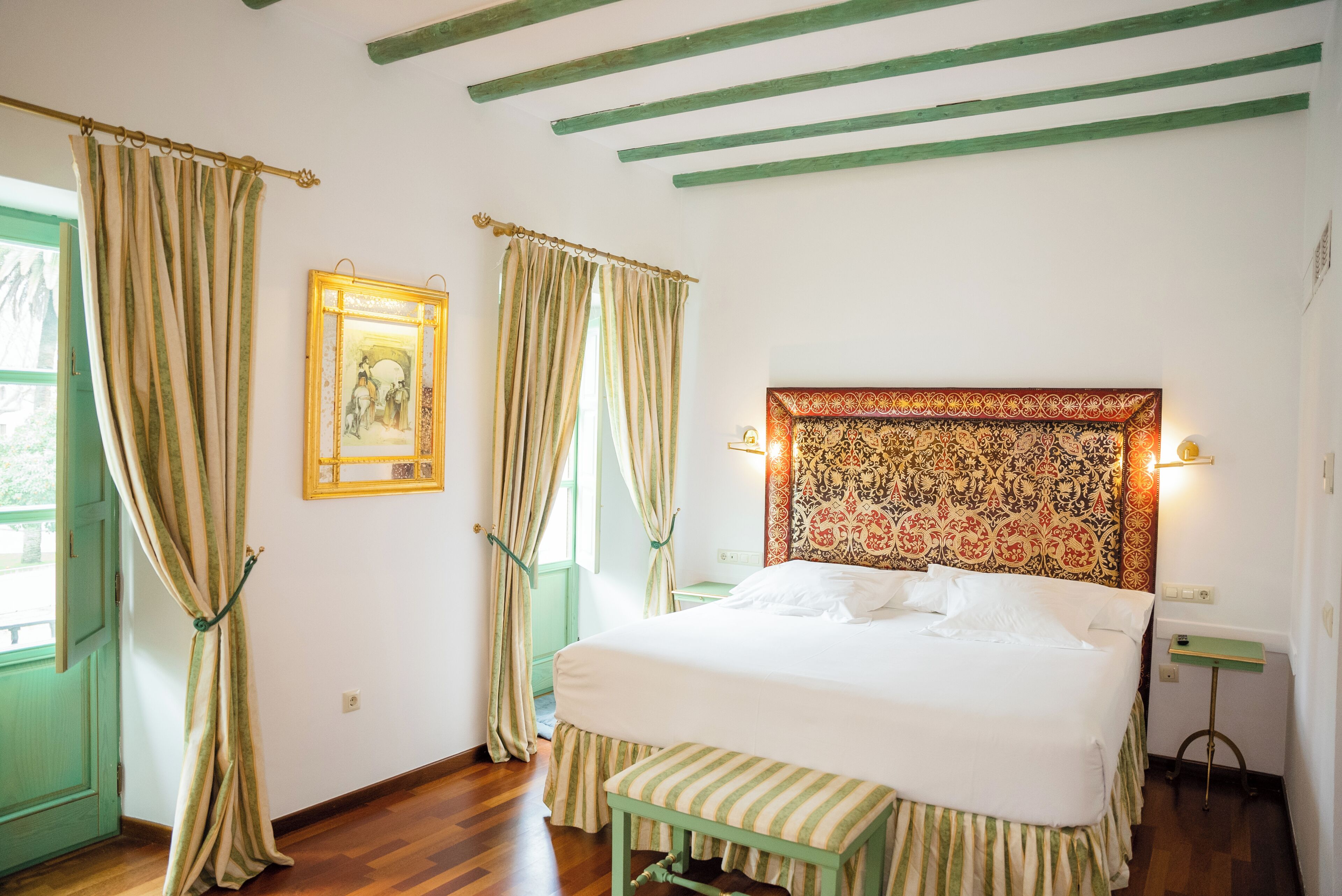 Une chambre à coucher avec un lit, des rideaux, un tableau au mur et une tête de lit à motifs.