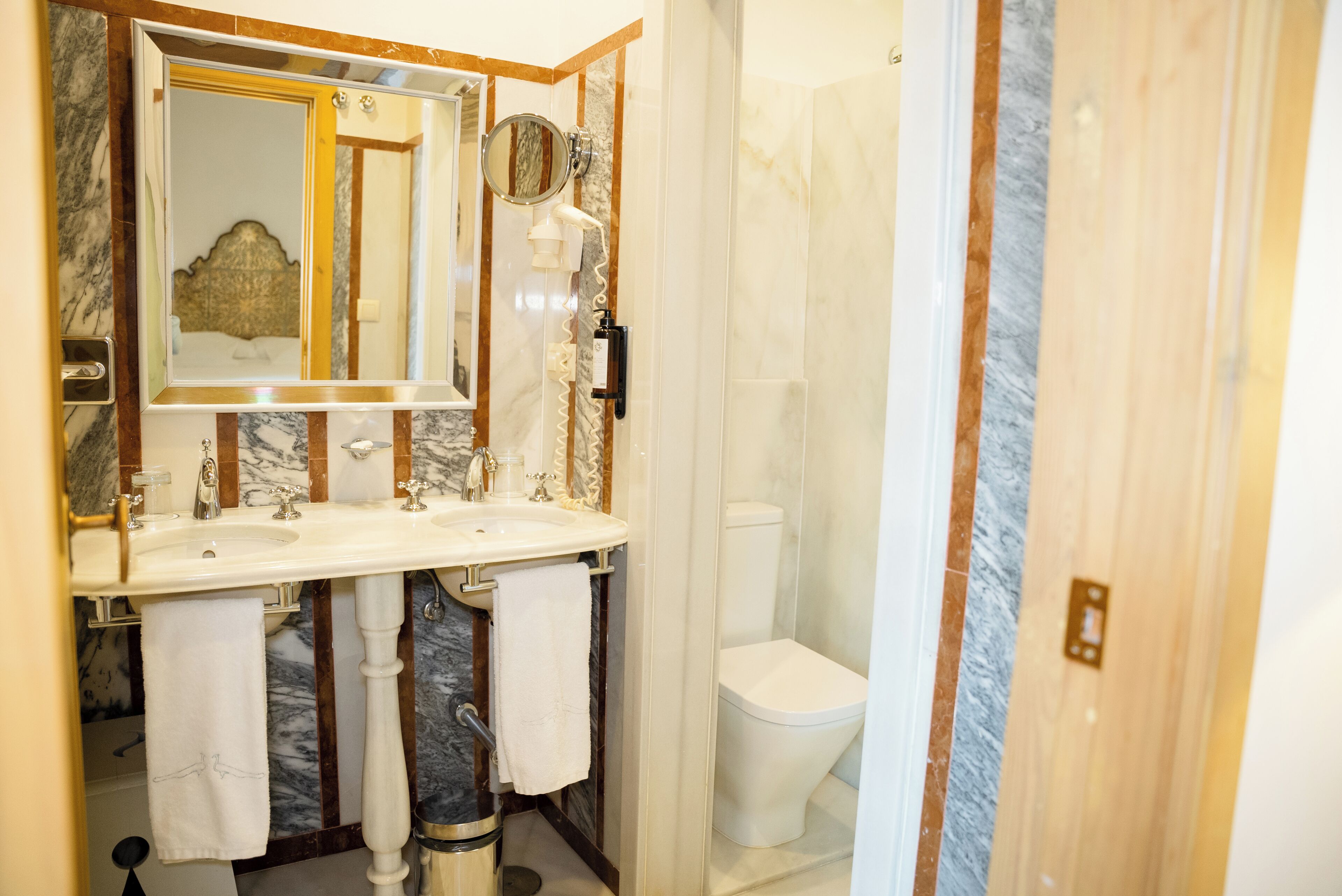 A bathroom with a marble vanity, a sink, a mirror, a towel rack, and a toilet.