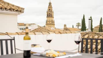 Una terraza con una mesa, dos copas de vino y una botella. Al fondo, una torre histórica y una palmera.