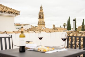 A terrace with a table, two wine glasses, and a bottle of wine. In the background, there is a historic tower and a palm tree. - Las Casas de la Judería de Córdoba (Córdoba)