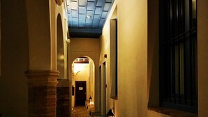 Un pasillo estrecho con suelo de baldosas, un banco y faroles que iluminan.