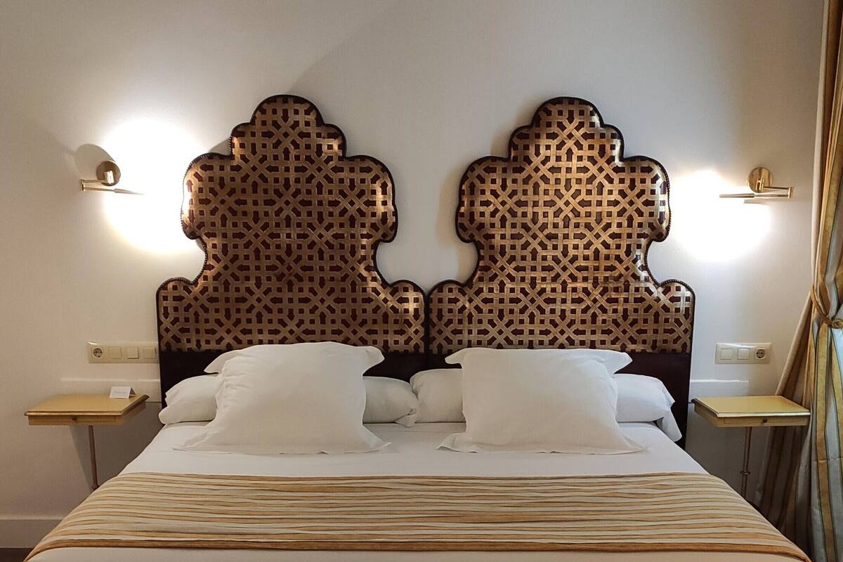 A neatly made bed with a striped bedspread, a wooden bench at the foot of the bed, and a decorative headboard with a lattice pattern.