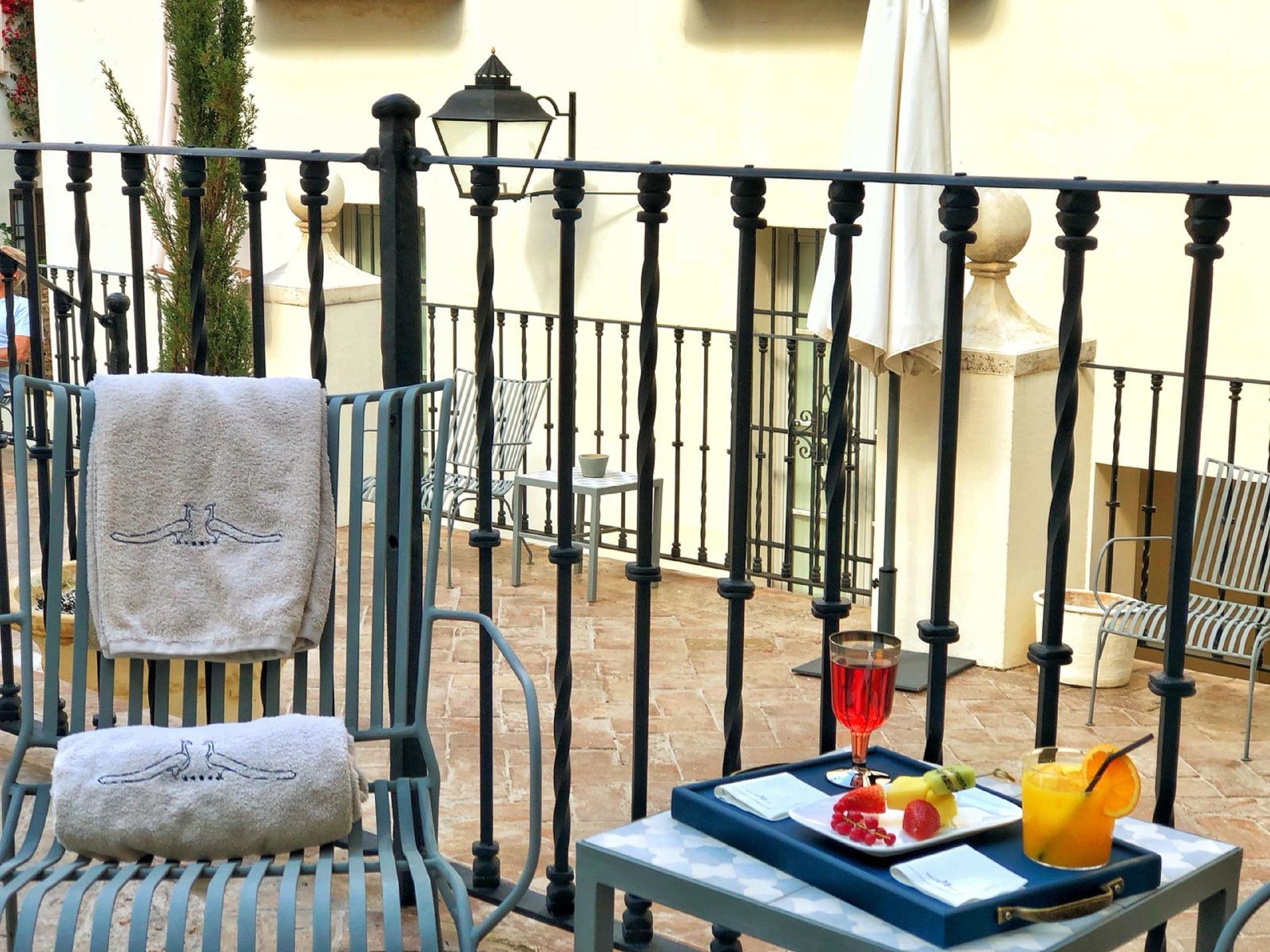 A balcony with a table set with fruit and a drink, chairs with towels, and a decorative lamp.