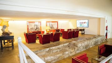 A room with a stone wall, red chairs, a table with a lamp, and a television screen.