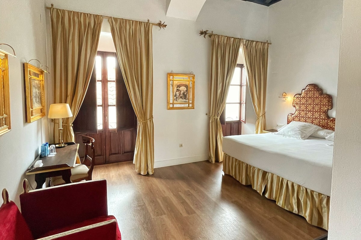 A hotel room with a bed, a desk, a chair, and a red sofa.