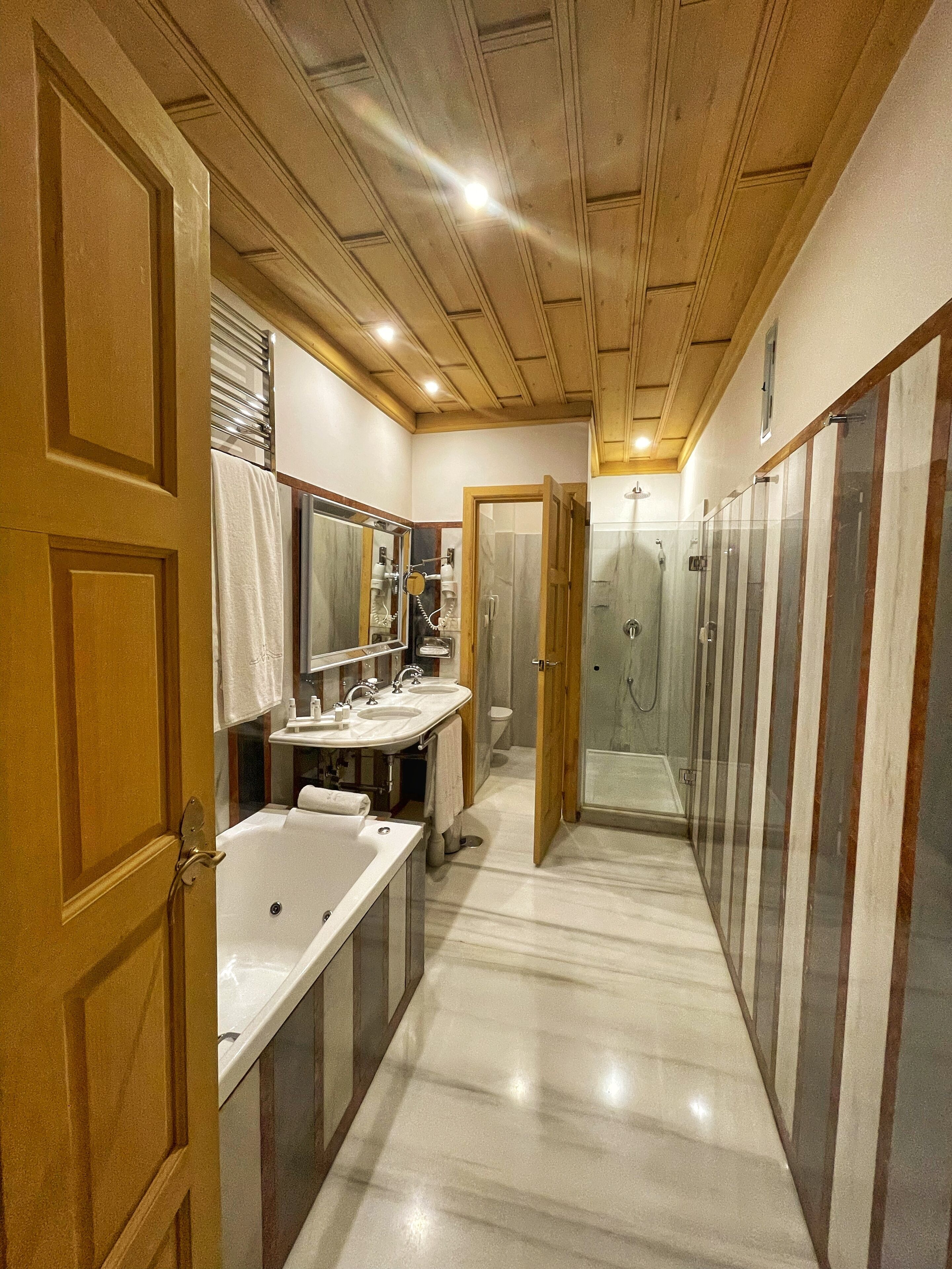 A modern bathroom with a wooden ceiling, two sinks, a shower, and a glass-enclosed shower area.
