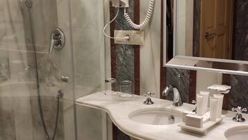 Un baño moderno con ducha de vidrio, tocador con dos lavamanos, un espejo grande y un secador de pelo en la pared.