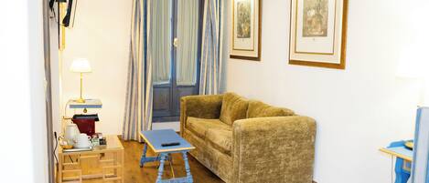 A room with a sofa, a small table, a lamp, and two framed pictures on the wall.