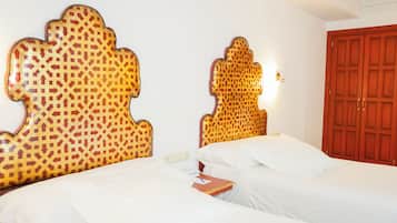 Une chambre d’hôtel avec deux lits, chacun doté d’une tête de lit à motifs, d’une table de chevet avec un livre et d’une armoire en bois.