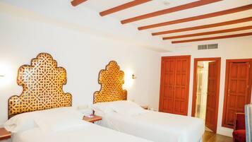 Habitación de hotel con dos camas individuales, cabeceros de madera, una mesita de noche y una silla roja.