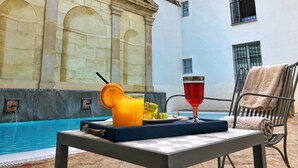 Mesa junto a la piscina con una bandeja que contiene un vaso de jugo de naranja, un vaso de bebida roja y un plato con fruta.
