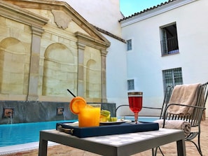 A poolside table with a tray containing a glass of orange juice, a glass of red drink, and a plate with fruit. - Las Casas de la Judería de Córdoba (Córdoba)