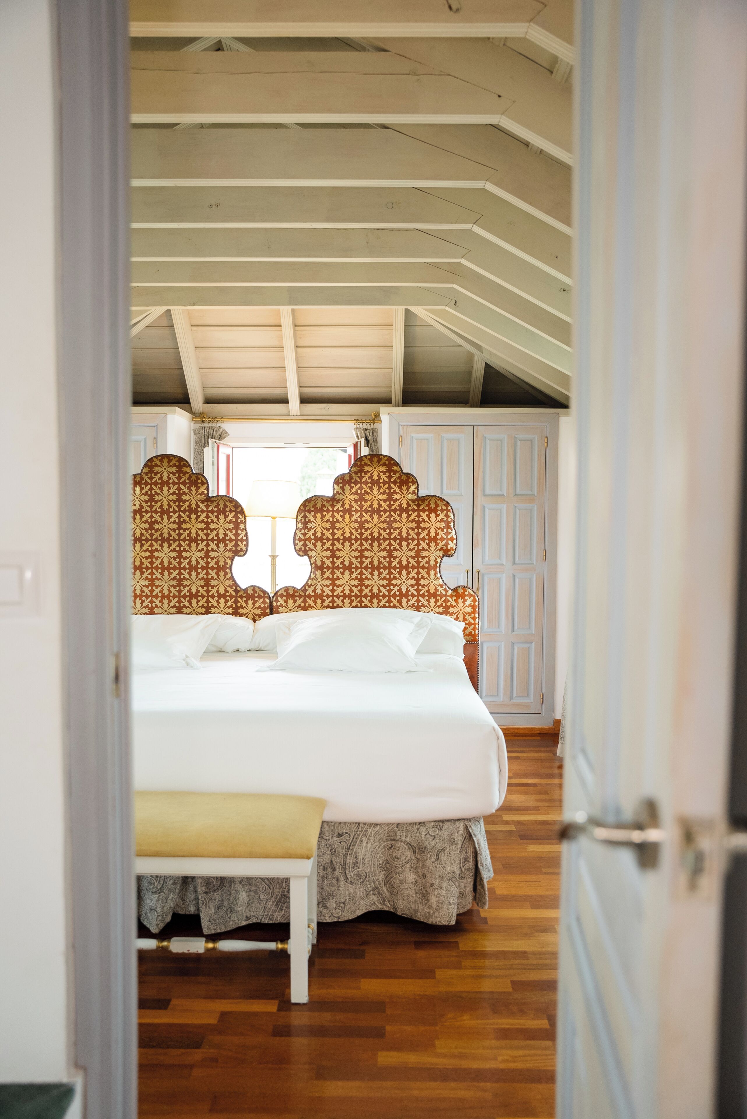 Un dormitorio con cama, una banca, cabeceros estampados y techo de madera.