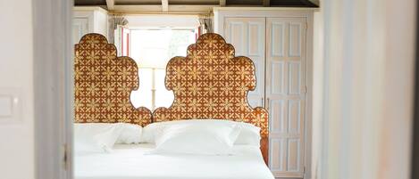 Un dormitorio con cama, una banca, cabeceros estampados y techo de madera.