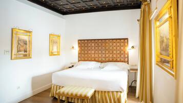 A hotel room with a large bed, a bench, a patterned headboard, and two framed pictures on the walls.