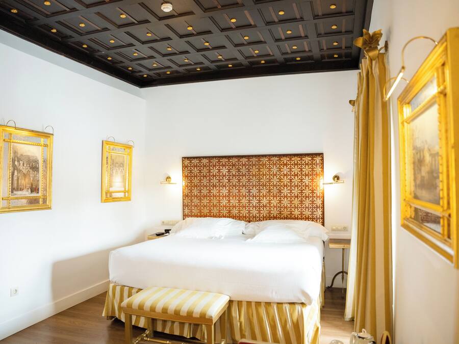 A hotel room with a large bed, a bench, a patterned headboard, and two framed pictures on the walls.