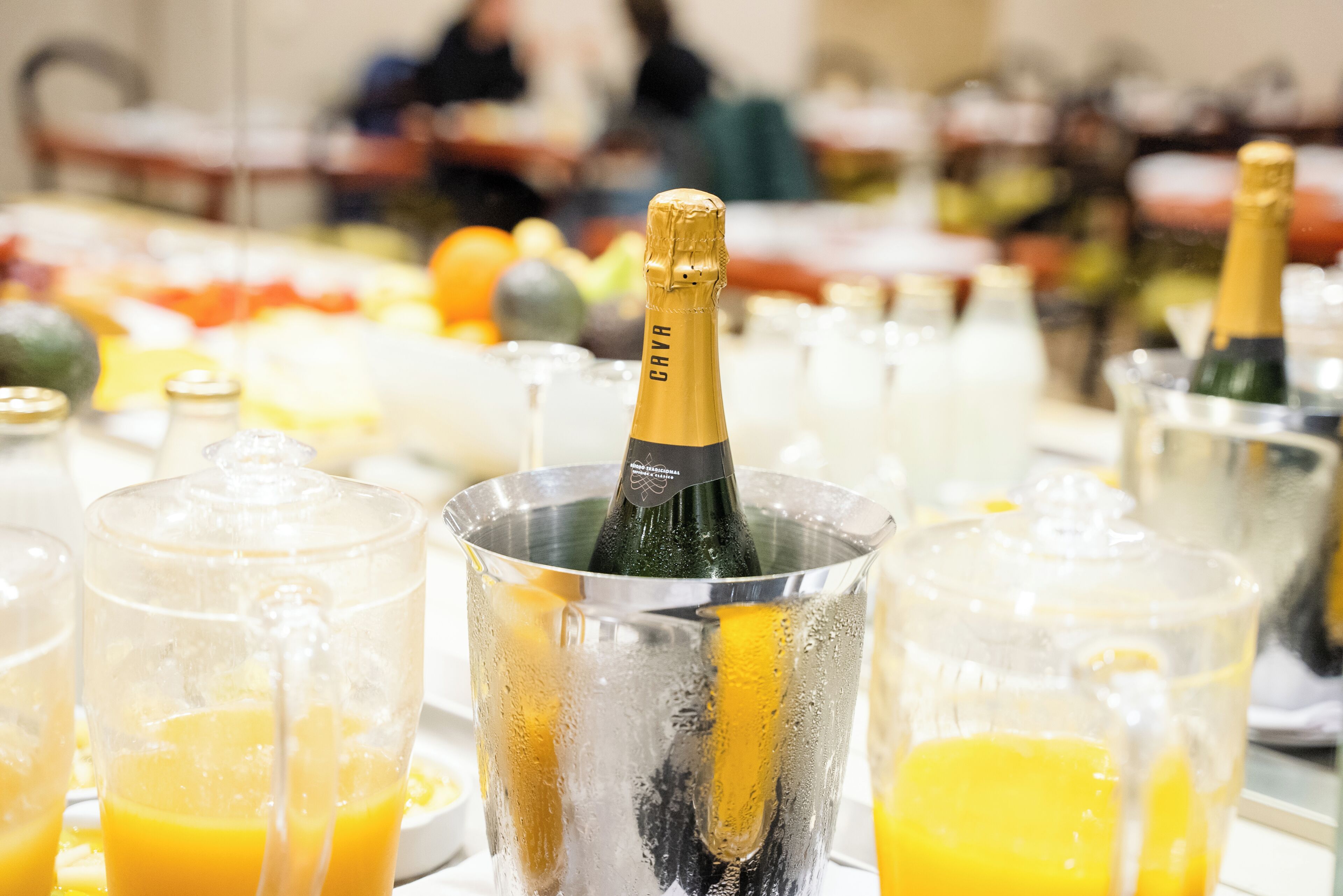Een champagnefles in een metalen emmer, omringd door glazen jus d'orange.