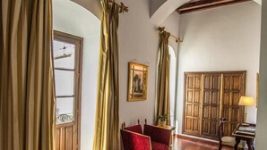 Una habitación de hotel con una cama, un sillón rojo, una puerta de madera y una ventana con cortinas.