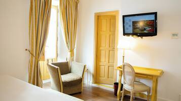 Une chambre d’hôtel comprenant un lit, un bureau, une chaise, un téléviseur fixé au mur et une porte.