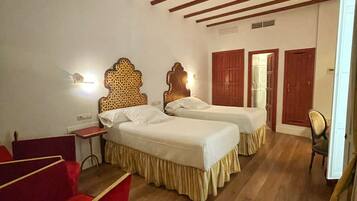 Habitación de hotel con dos camas, un sofá rojo, suelo de madera y techo con vigas a la vista.